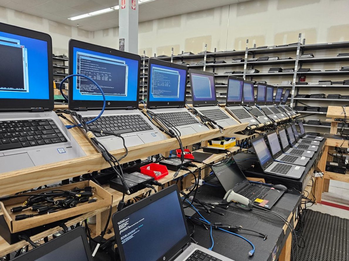 Laptops cabled side by side on a wiping bench in Florence, Kentucky, their screens showing the wipe running.