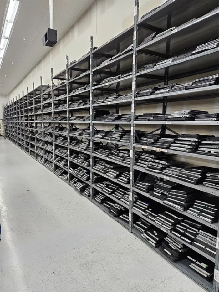 A long aisle of shelving on the Regadget floor, stacked with refurbished laptops.