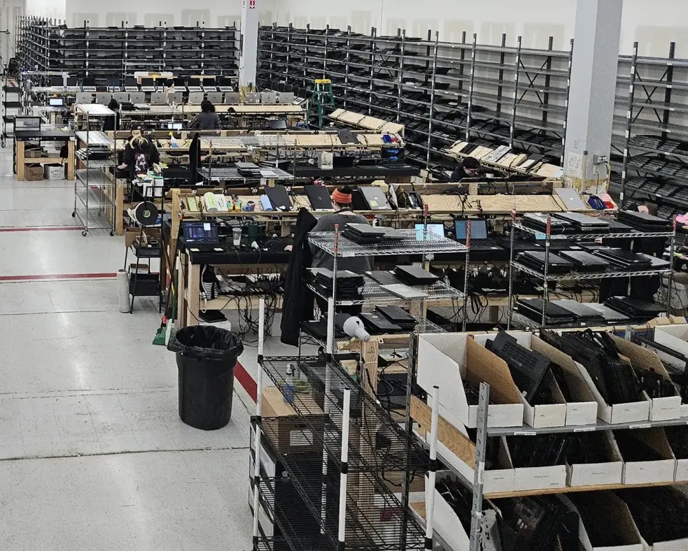 Technicians at benches on the processing floor in Florence, Kentucky, with bins and racks of retired laptops around them.
